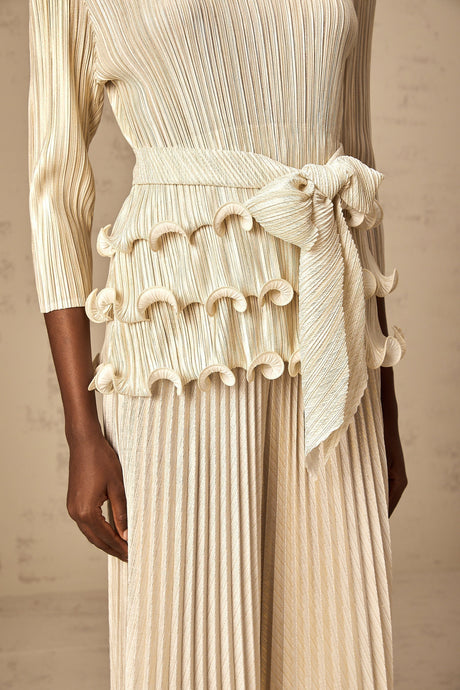 A woman wearing a white jumpsuit with floral appliques ruffles and pleated details