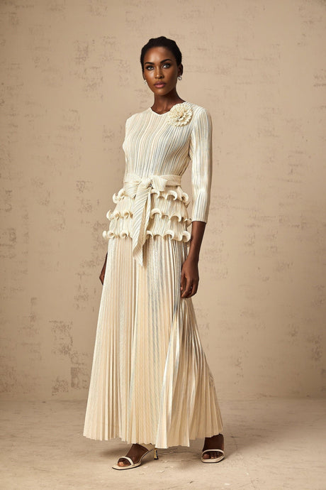 A woman wearing a white jumpsuit with floral appliques ruffles and pleated details