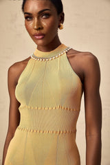 A woman wearing a white knit midi dress with faux pearl embellishments on the bodice and sleeves standing in a neutral background