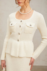 A woman wearing a white knitted crop top and matching skirt set standing against a plain background