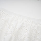 A woman wearing a white lace trimmed cropped top and matching trousers The top features cutout details and the set has a delicate feminine design