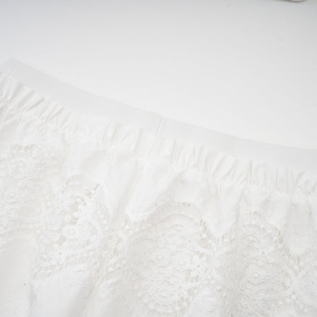 A woman wearing a white lace trimmed cropped top and matching trousers The top features cutout details and the set has a delicate feminine design