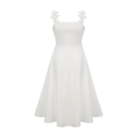 A woman wearing a white midi dress with a square neckline and faux flower embellishments standing against a plain background