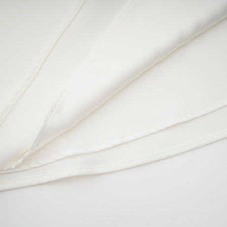 A woman wearing a white midi dress with a square neckline and faux flower embellishments standing in a neutral background