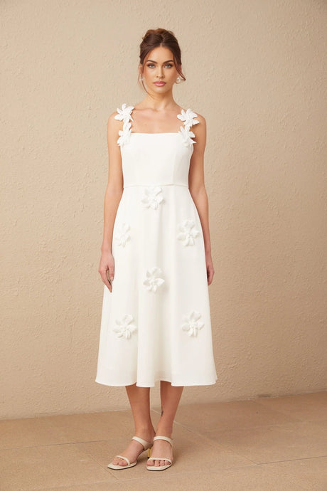A woman wearing a white midi dress with a square neckline and faux flower embellishments standing in a neutral pose
