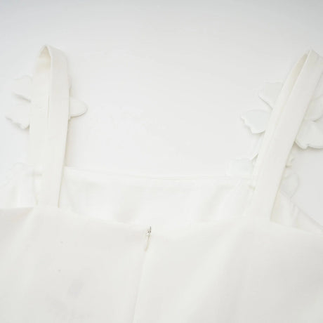 A woman wearing a white midi dress with a square neckline and faux flower embellishments standing in a relaxed pose