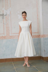 A woman wearing a white midi dress with cap sleeves and an open back design standing in a relaxed pose