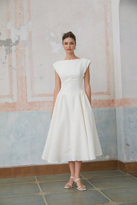 A woman wearing a white midi dress with cap sleeves and an open back design standing in a relaxed pose