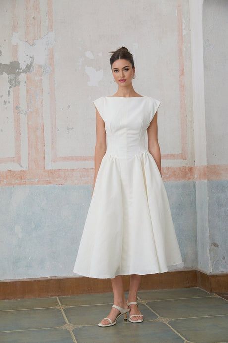 A woman wearing a white midi dress with cap sleeves and an open back design standing in a relaxed pose