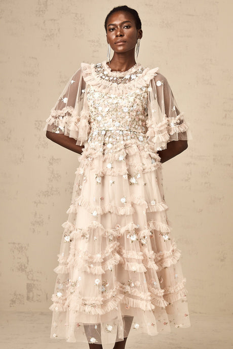 A woman wearing a white midi dress with tiered ruffles and floral embroidery standing in a garden setting