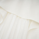 A woman wearing a white offshoulder maxi dress with pleated details the dress has a flowy silhouette and extends to the floor