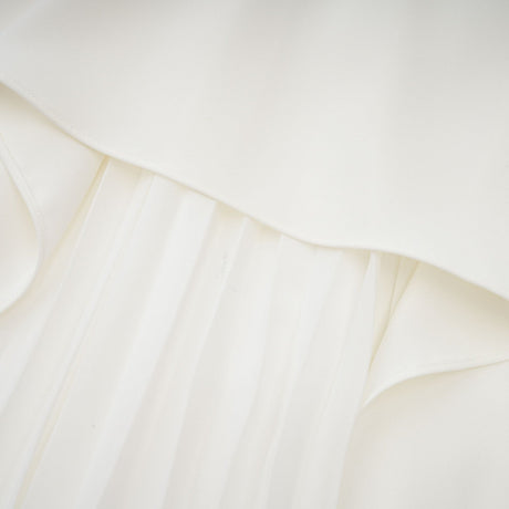 A woman wearing a white offshoulder maxi dress with pleated details the dress has a flowy silhouette and extends to the floor