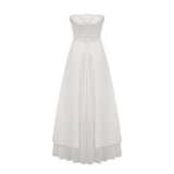 A woman wearing a white pleated offshoulder maxi dress with a flowing skirt standing against a plain background