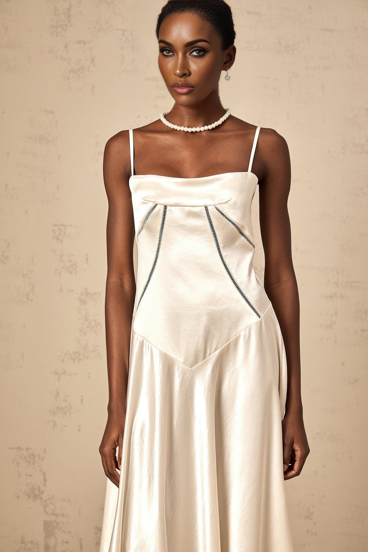 A woman wearing a white satin maxi dress with a flared skirt and sleek silhouette standing against a plain background