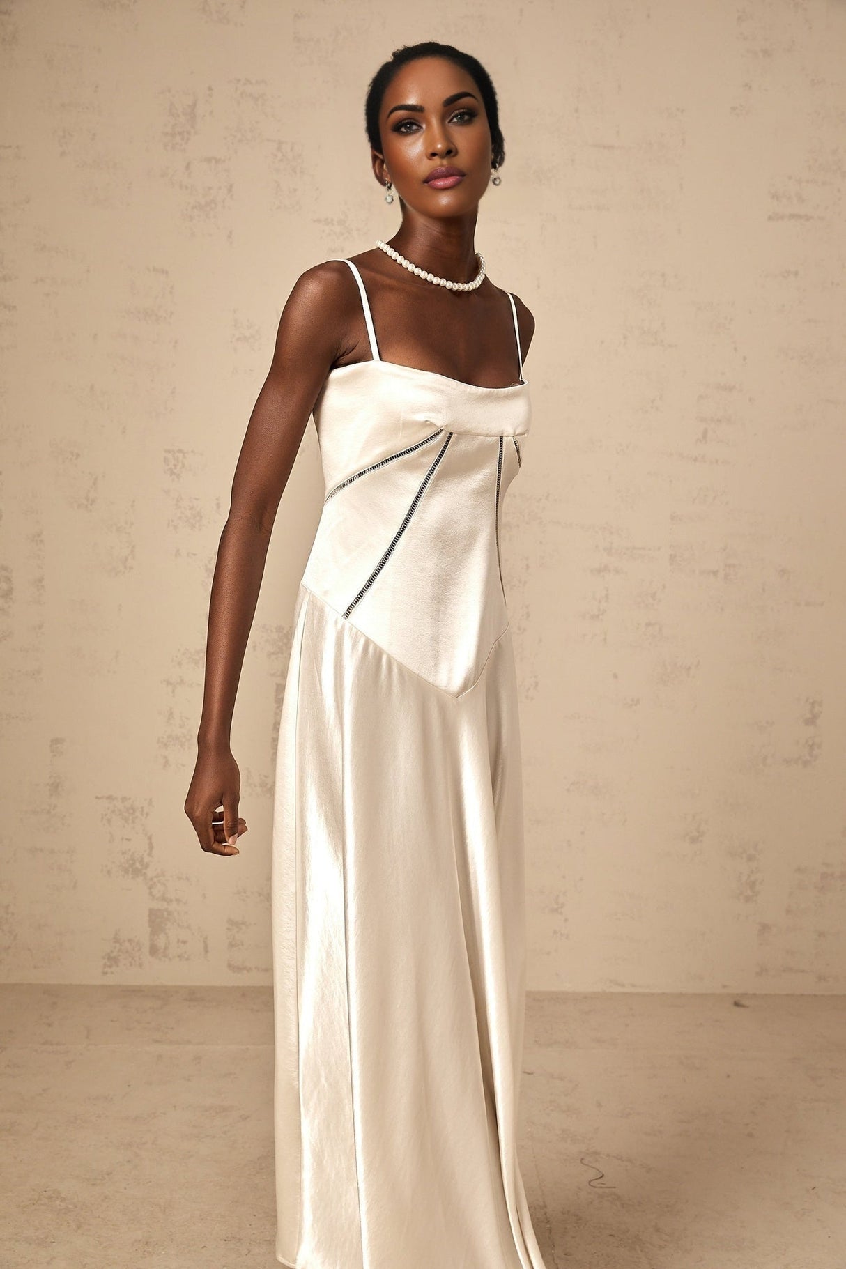 A woman wearing a white satin maxi dress with a flared skirt standing against a plain background