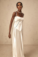 A woman wearing a white satin maxi dress with a flared skirt standing against a plain background