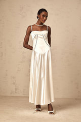 A woman wearing a white satin maxi dress with a flared skirt standing against a plain background