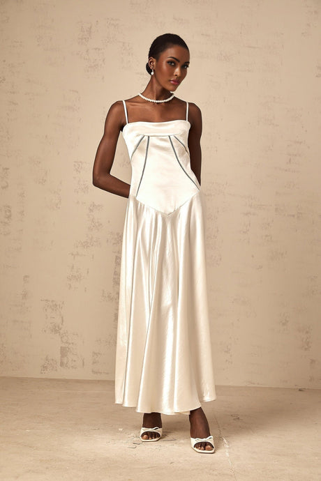 A woman wearing a white satin maxi dress with a flared skirt standing against a plain background