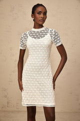 A woman wearing a white semisheer knit mini dress standing in a casual pose