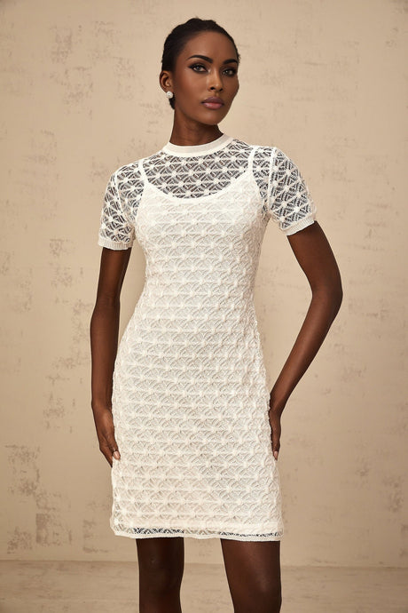 A woman wearing a white semisheer knit mini dress standing in a casual pose
