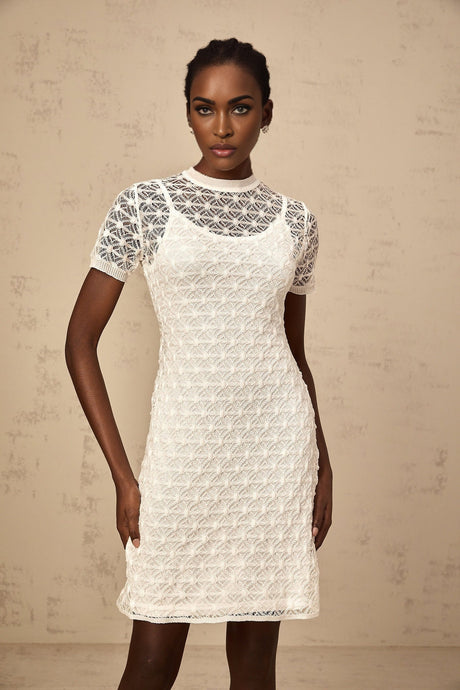 A woman wearing a white semisheer knit mini dress with short sleeves and a formfitting silhouette