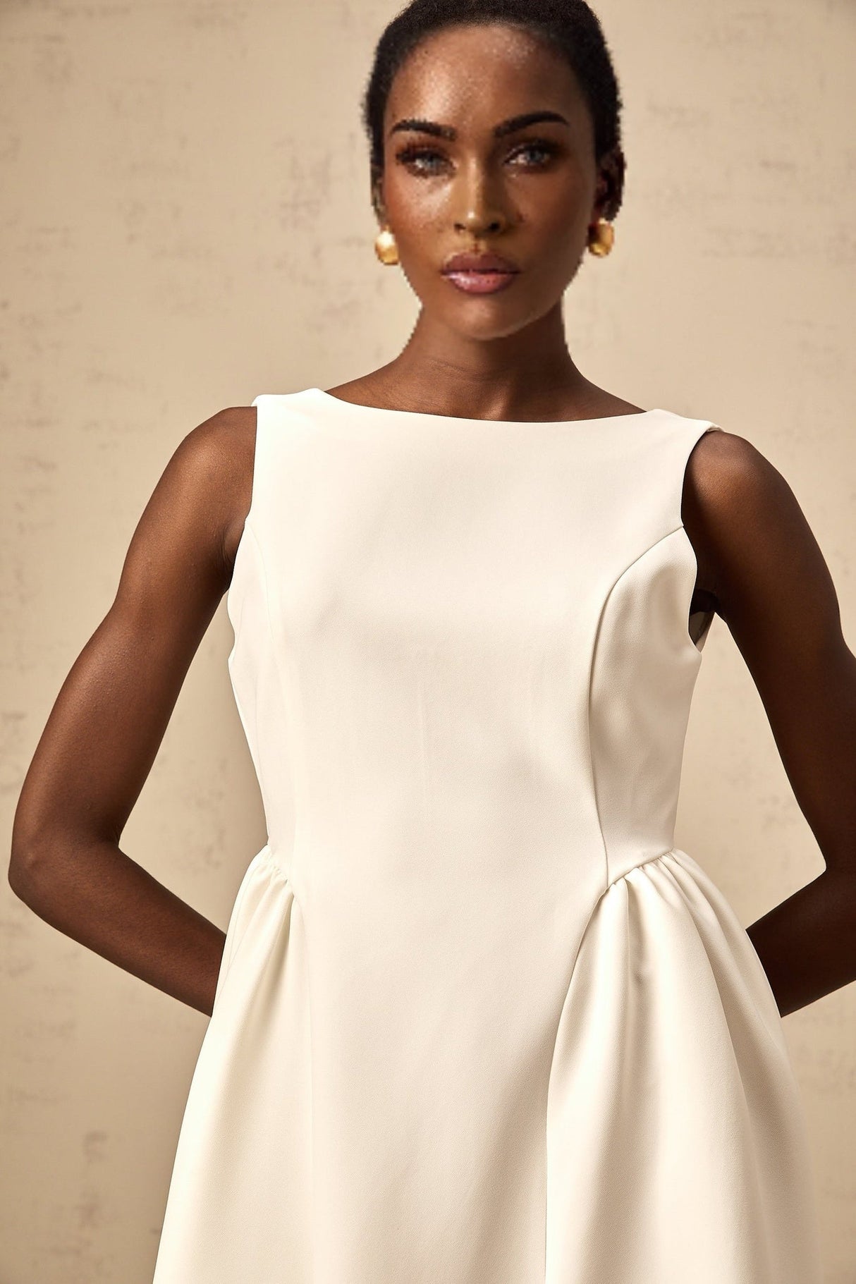 A woman wearing a white sleeveless midi dress with a full skirt standing against a plain background