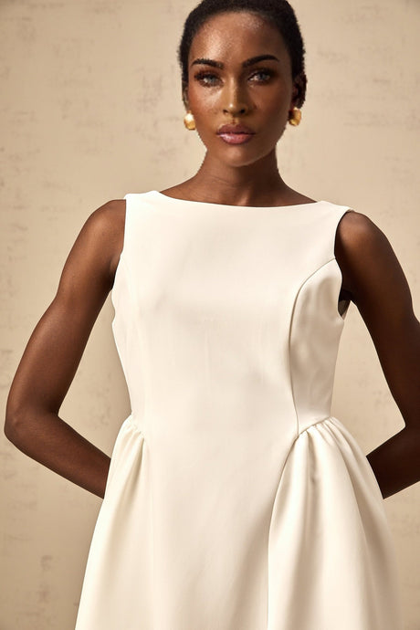 A woman wearing a white sleeveless midi dress with a full skirt standing against a plain background