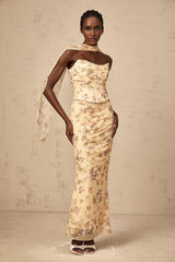 A woman wearing a yellow floral print matching set consisting of a fitted top and skirt standing against a plain background