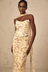 A woman wearing a yellow floral print matching set consisting of a fitted top and skirt standing against a plain background