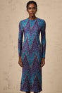 A woman wearing a zigzag patterned knitted midi dress with long sleeves standing against a plain background