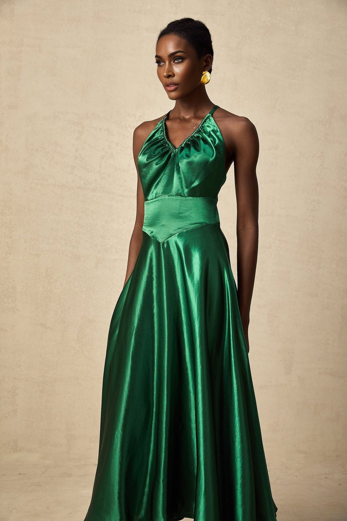 A woman wearing an emerald green satin midi dress with an open back design standing in a neutral background