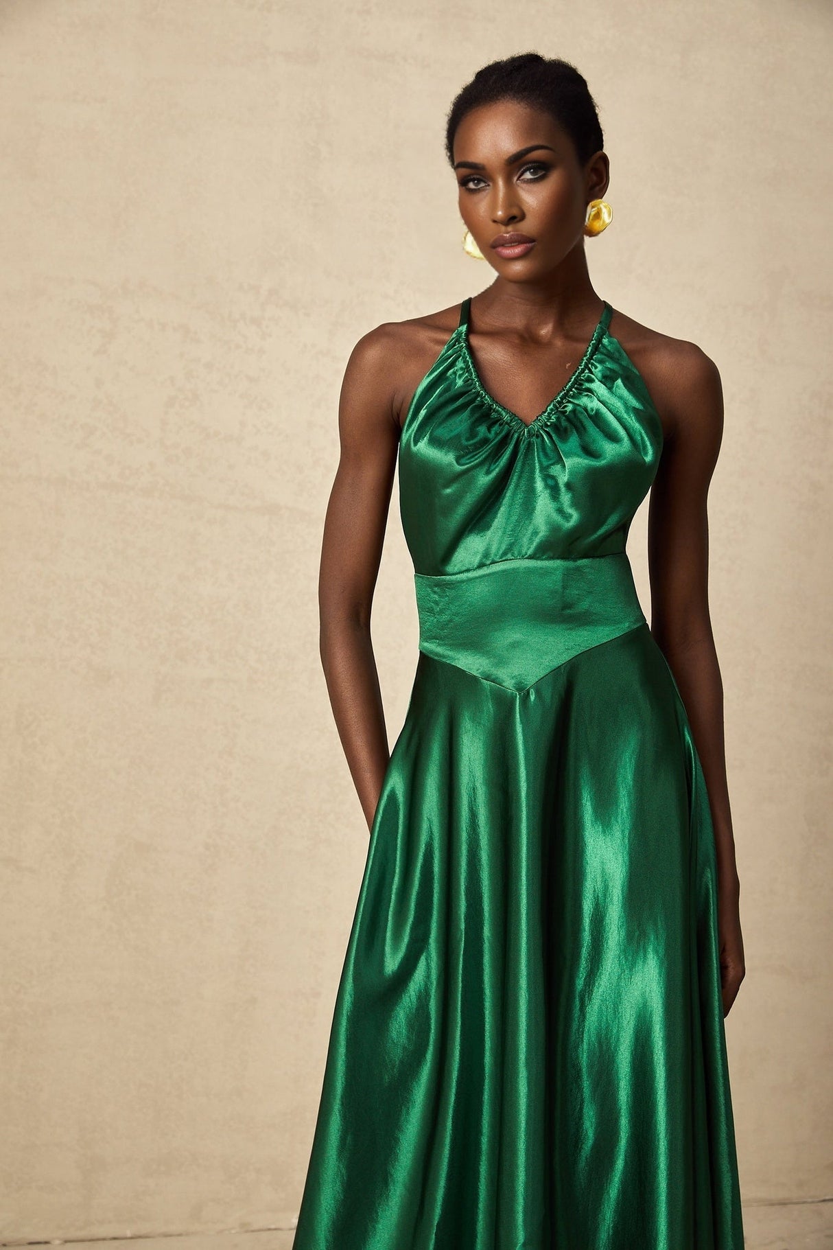 A woman wearing an emerald green satin midi dress with an open back design