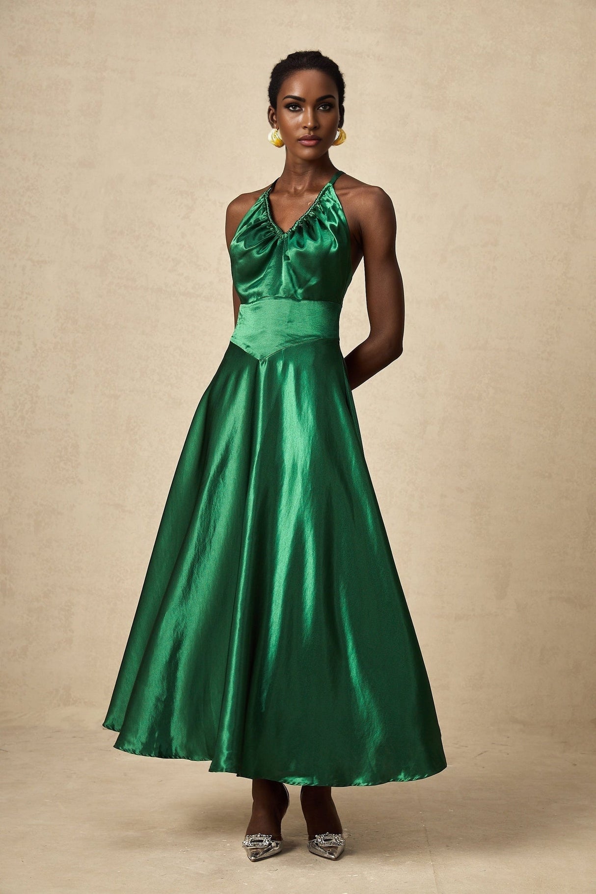 A woman wearing an emerald green satin midi dress with an open back design