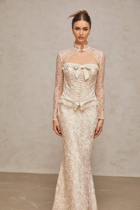 A woman wearing an ivory colored matching set consisting of a patterned jacquard top and skirt the set features a textured floral design and a coordinated elegant look