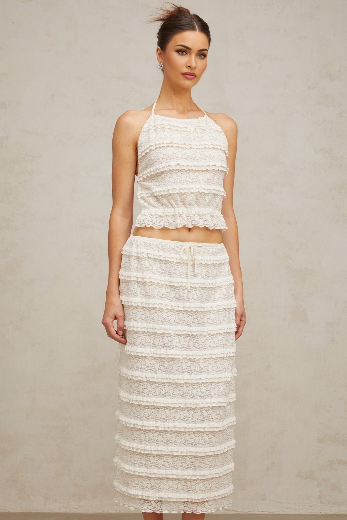A woman wearing an off white floral lace matching set consisting of a ruffled top and skirt The outfit has delicate lace details and a feminine ruffled design