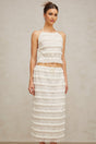 A woman wearing an off white floral lace matching set consisting of a ruffled top and skirt The outfit has delicate lace details and a feminine ruffled design