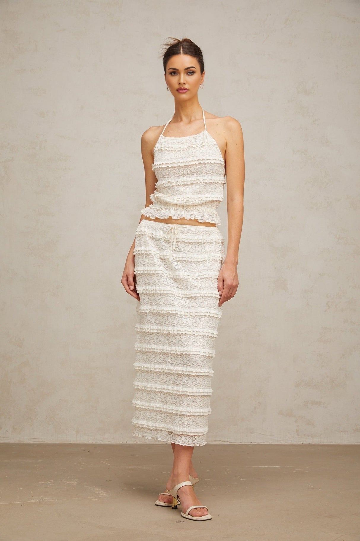 A woman wearing an off white floral lace matching set consisting of a ruffled top and skirt the top has short sleeves and the skirt falls to mid thigh length