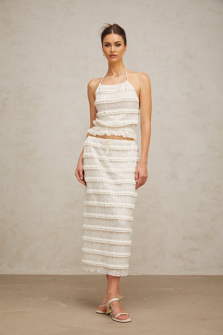 A woman wearing an off white floral lace matching set consisting of a ruffled top and skirt the top has short sleeves and the skirt falls to mid thigh length