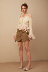 A woman wearing an offshoulder tweed top with feather trim detailing around the neckline and sleeves The top has a fitted silhouette and appears to be in a light color