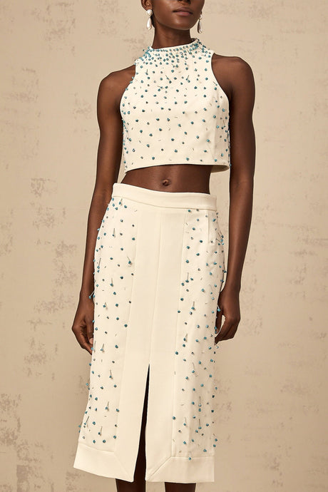 A woman wearing an offwhite matching set consisting of an embellished top and skirt named Clothilde The top features delicate embroidery while the skirt has a flowing design Both pieces are coordinated in color and style creating an elegant ensemble