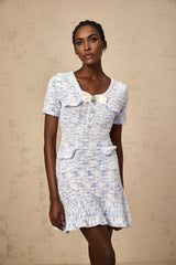 A young woman wearing a blue and white checked knit mini dress with short sleeves and a fitted silhouette standing against a plain background
