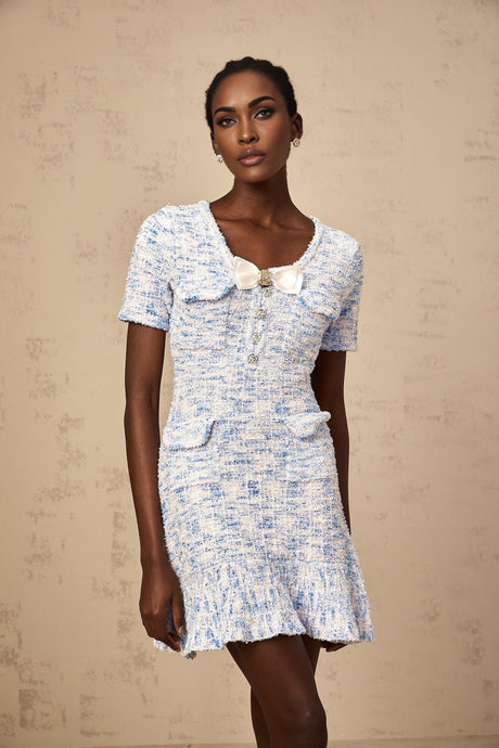 A young woman wearing a blue and white checked knit mini dress with short sleeves and a fitted silhouette standing against a plain background