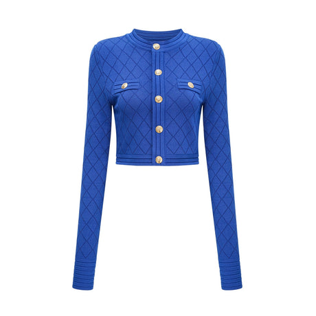 A young woman wearing a blue knitted two piece outfit consisting of a long sleeve top with button details and a matching skirt