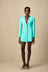 A young woman wearing a green mini blazer dress with a cinched waist standing in a casual pose