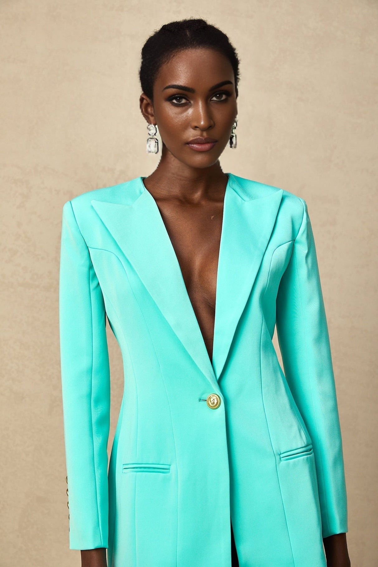 A young woman wearing a green mini blazer dress with a cinched waist the dress features lapels and buttons like a blazer but is styled as a short dress