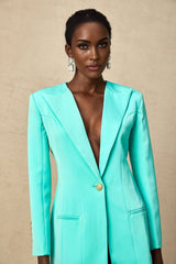 A young woman wearing a green mini blazer dress with a cinched waist the dress features lapels and buttons like a blazer but is styled as a short dress
