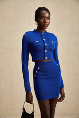 A young woman wearing a light blue knitted matching set consisting of a long sleeve top with button details and a skirt