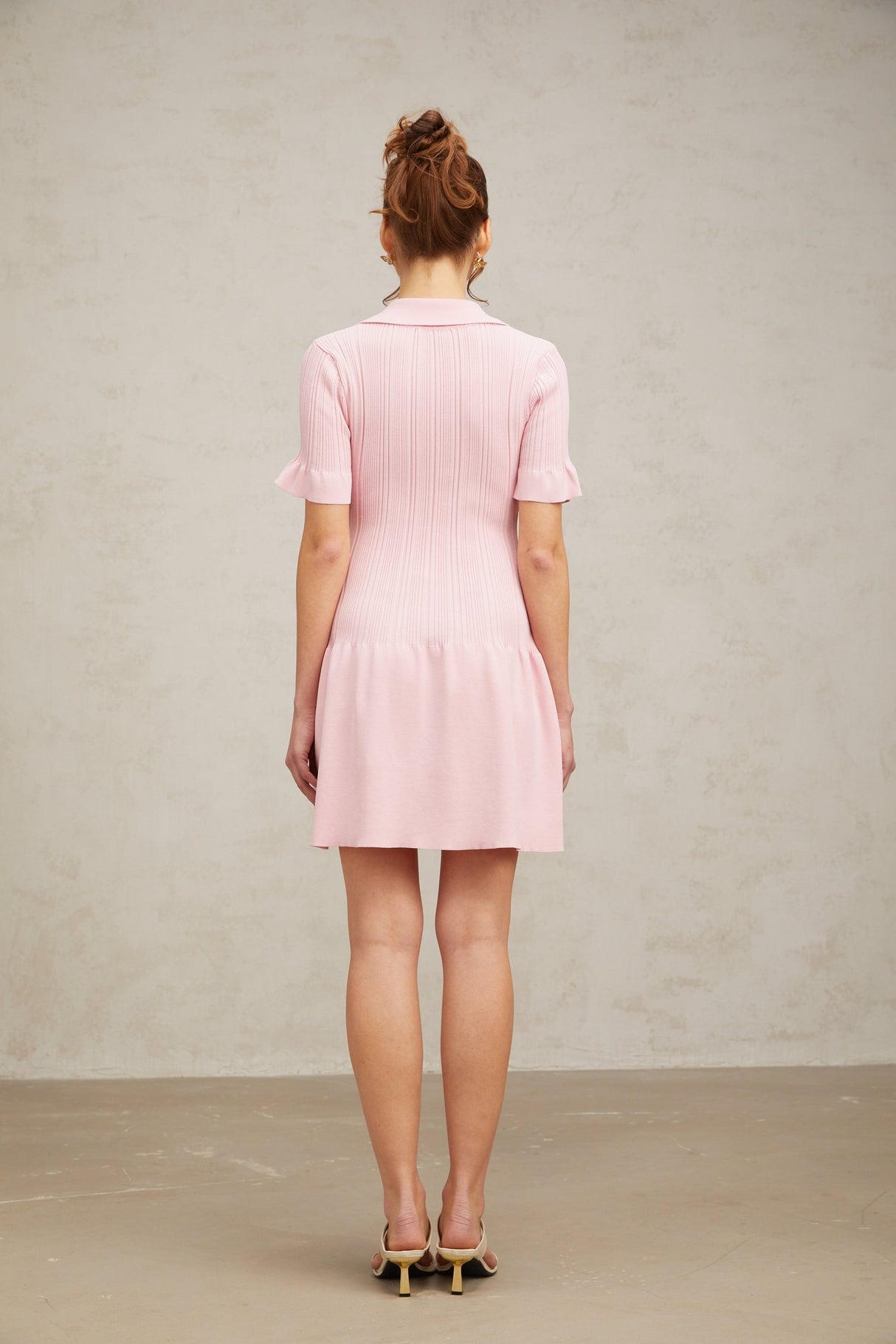 A young woman wearing a pink mini dress with a flared skirt and long sleeves made from fine knit fabric