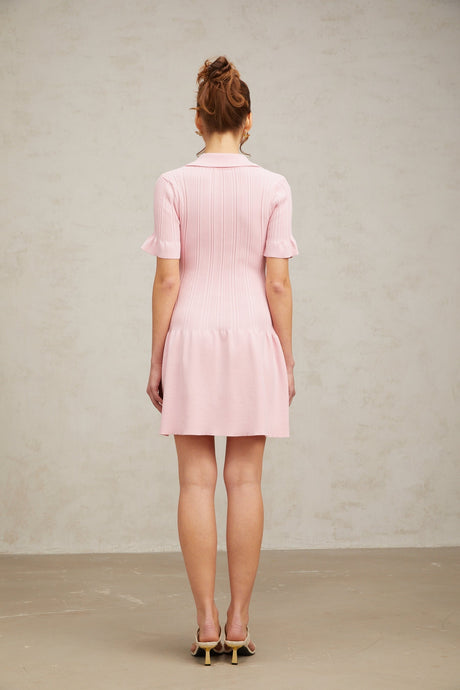 A young woman wearing a pink mini dress with a flared skirt and long sleeves made from fine knit fabric