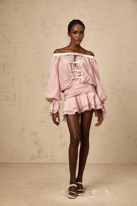 A young woman wearing a pink offshoulder mini dress with a bow detail and flounced hem